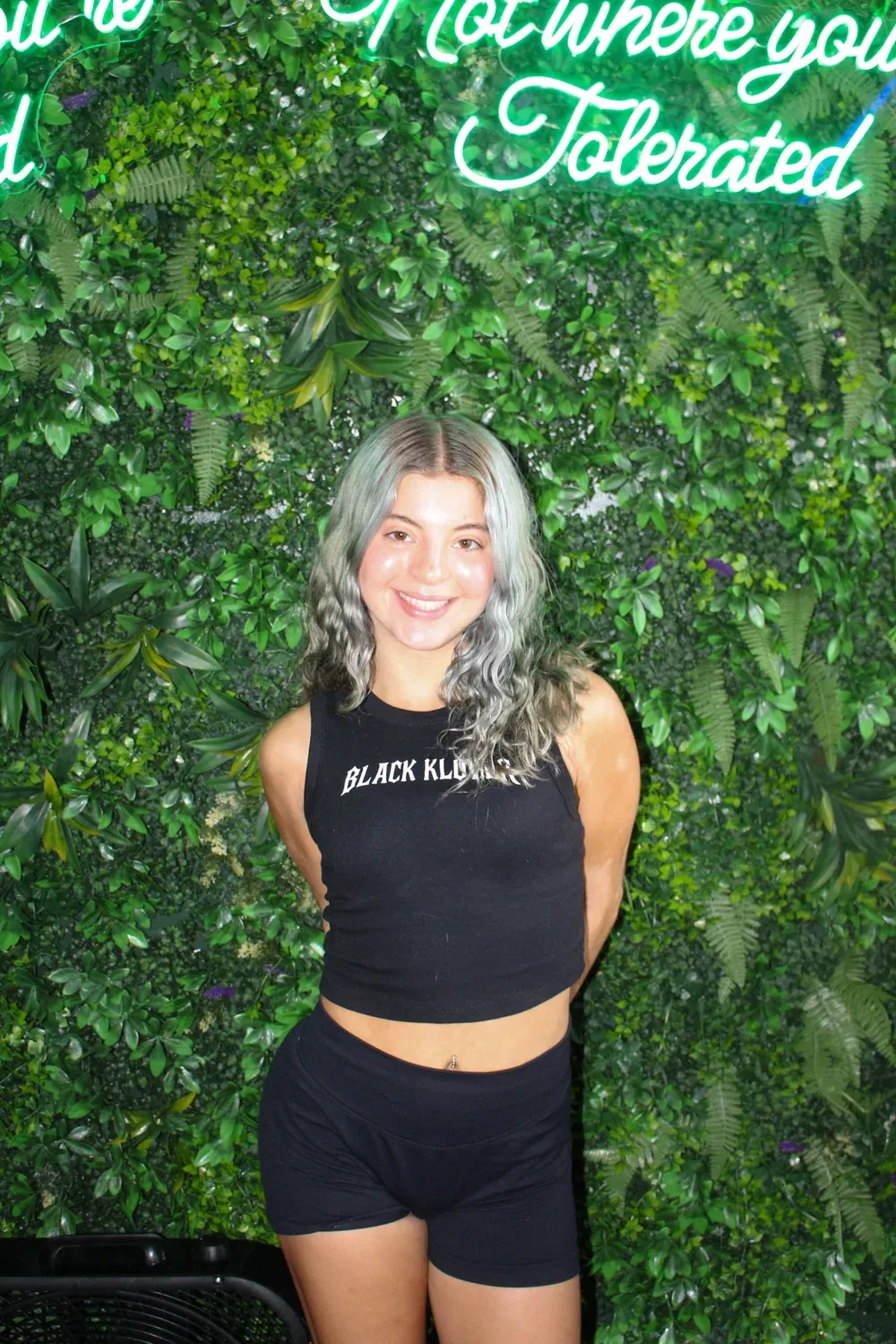 Sarah smiling against a greenery wall