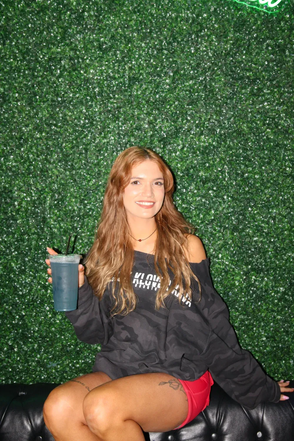 Vanessa holding a drink against the Black Klover greenery wall