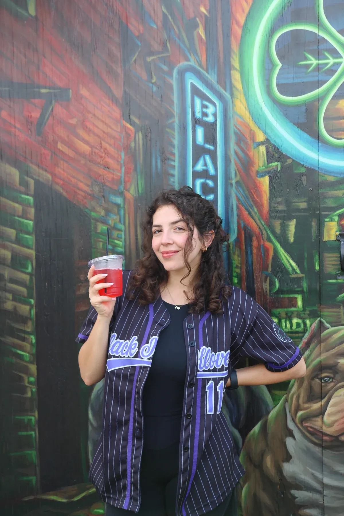Zayna holding a red drink in front of a Black Klover mural